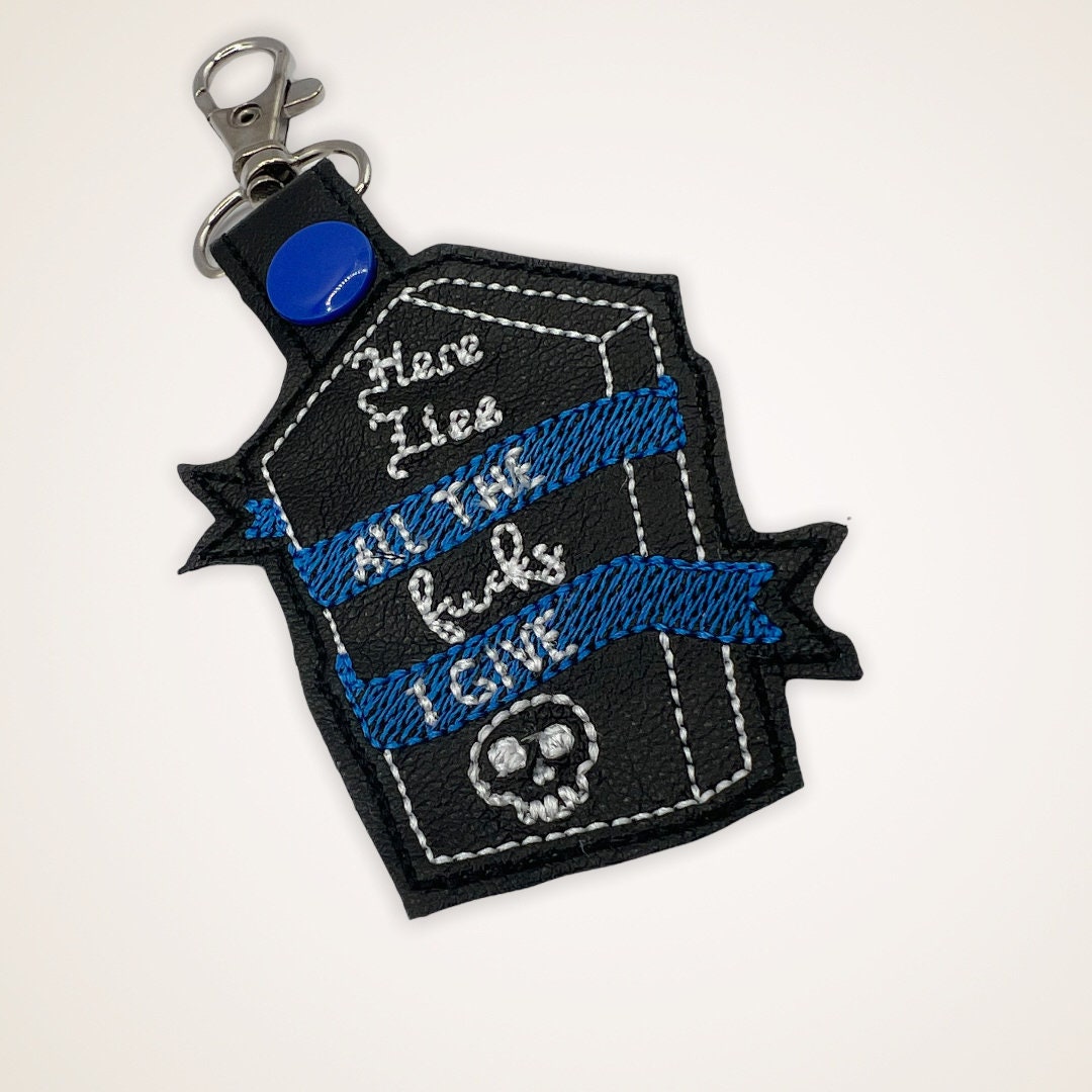 Embroidered Keychain that says Here Lies the Fucks I Give in a coffin shape