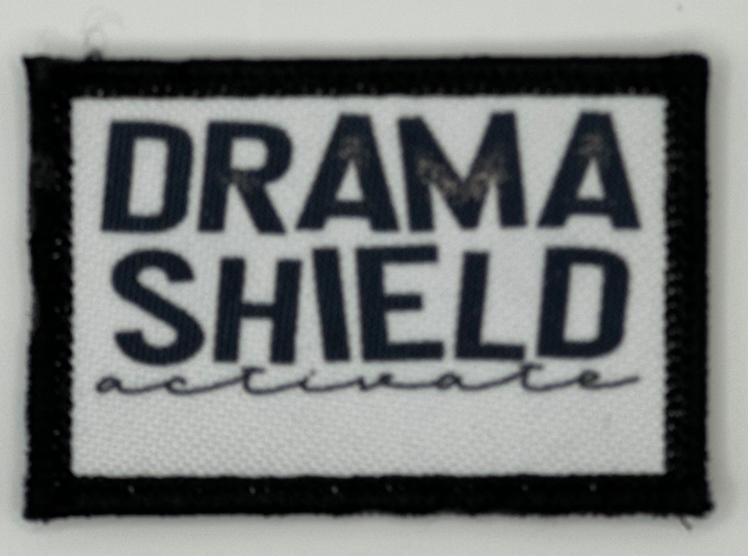 a black and white patch with the words drama shield on it